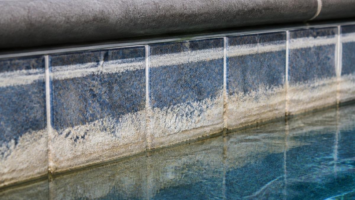 Pool Tile Cleaning Service Cost: 2026 Pricing Guide 1 Close-up of waterline tile showing white and gray calcium scale buildup on pool surface with mineral deposits visible on grout lines